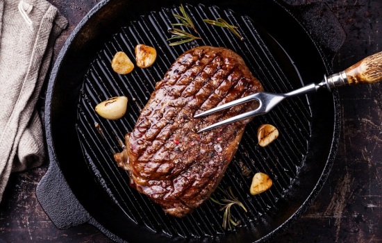 Grilled Ribeye steak and meat fork on grill pan on dark background